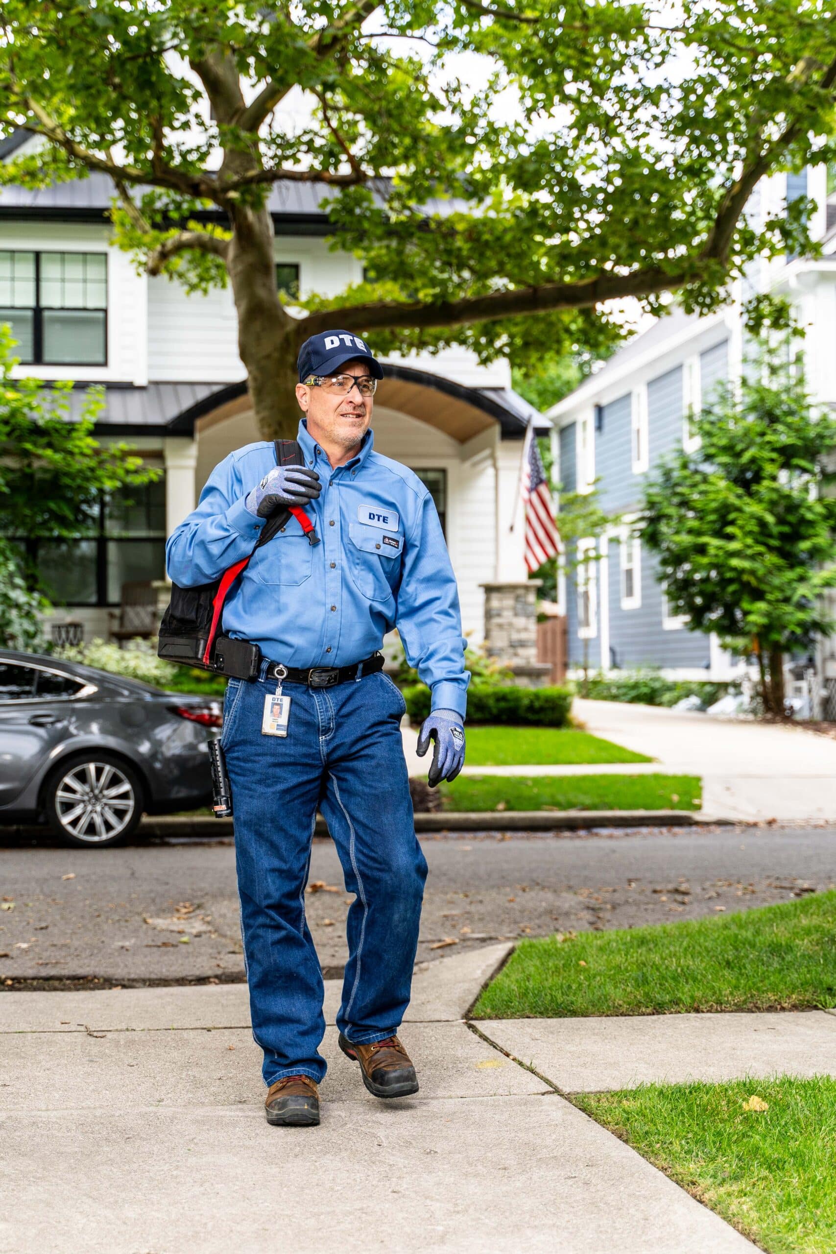Professional technician walking in suburban neighborhood with tools and uniform, American flag in background.